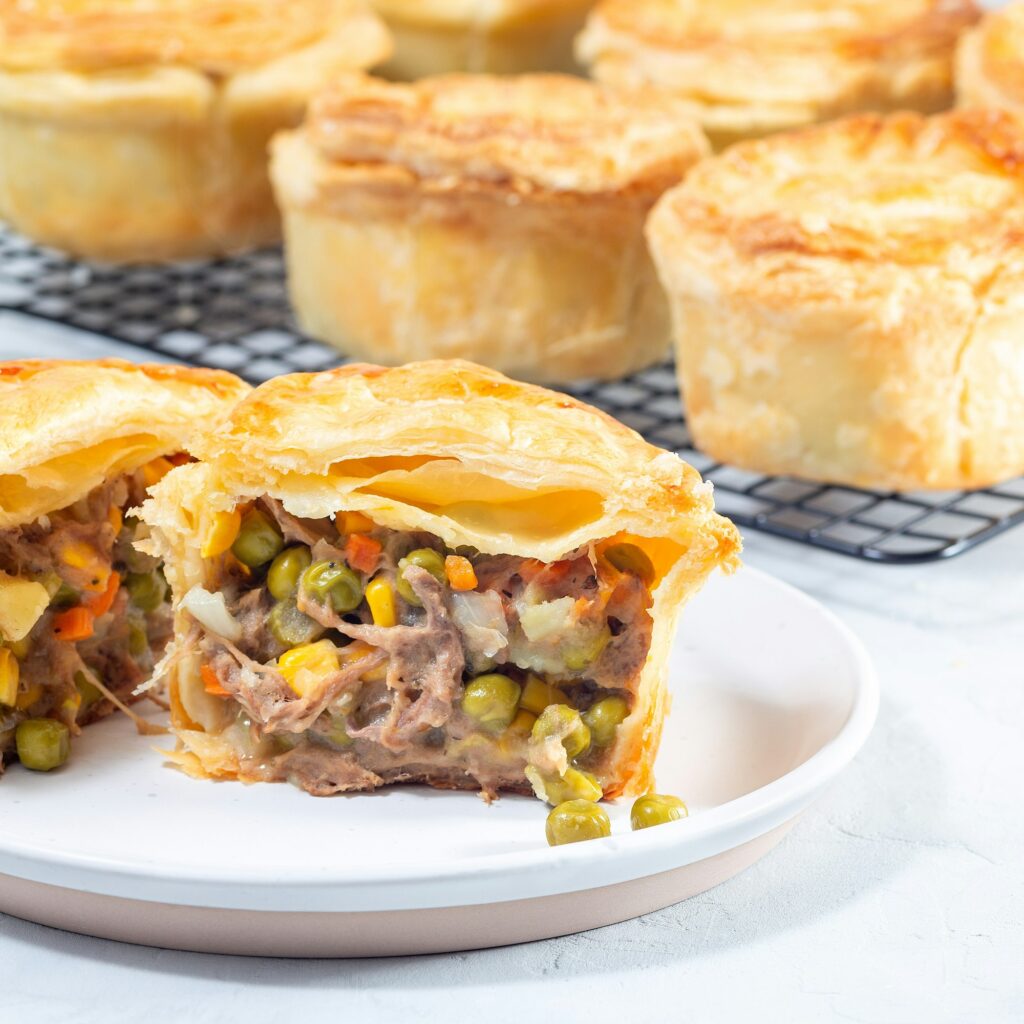 Sliced beef pot pie on plate, pies on cooling rack, square